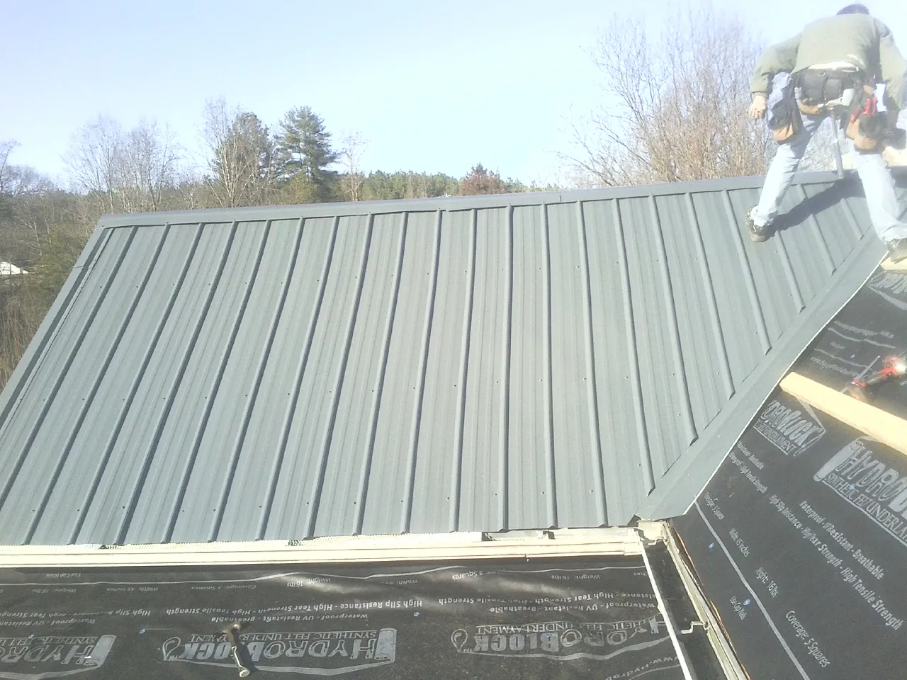 Crew installing dark green standing seam panels over synthetic underlayment in Dublin
